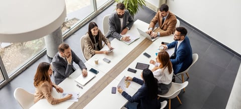Leadership team sitting at conference table in boardroom having quarterly business review meeting